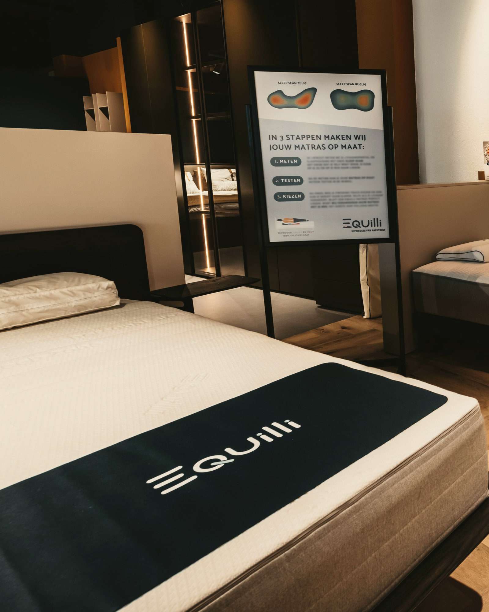 Een bed met een Equilli-matras in de showroom, naast een bord dat in drie stappen uitlegt hoe een matras op maat wordt gemaakt