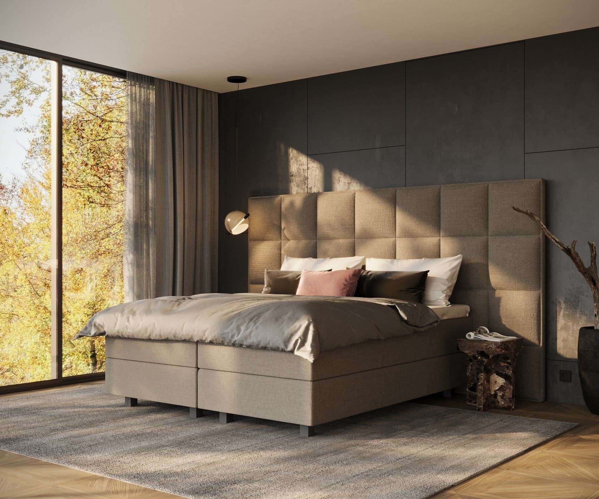 Een taupe boxspring met een hoog gestoffeerd hoofdbord in een slaapkamer met een grote glazen pui