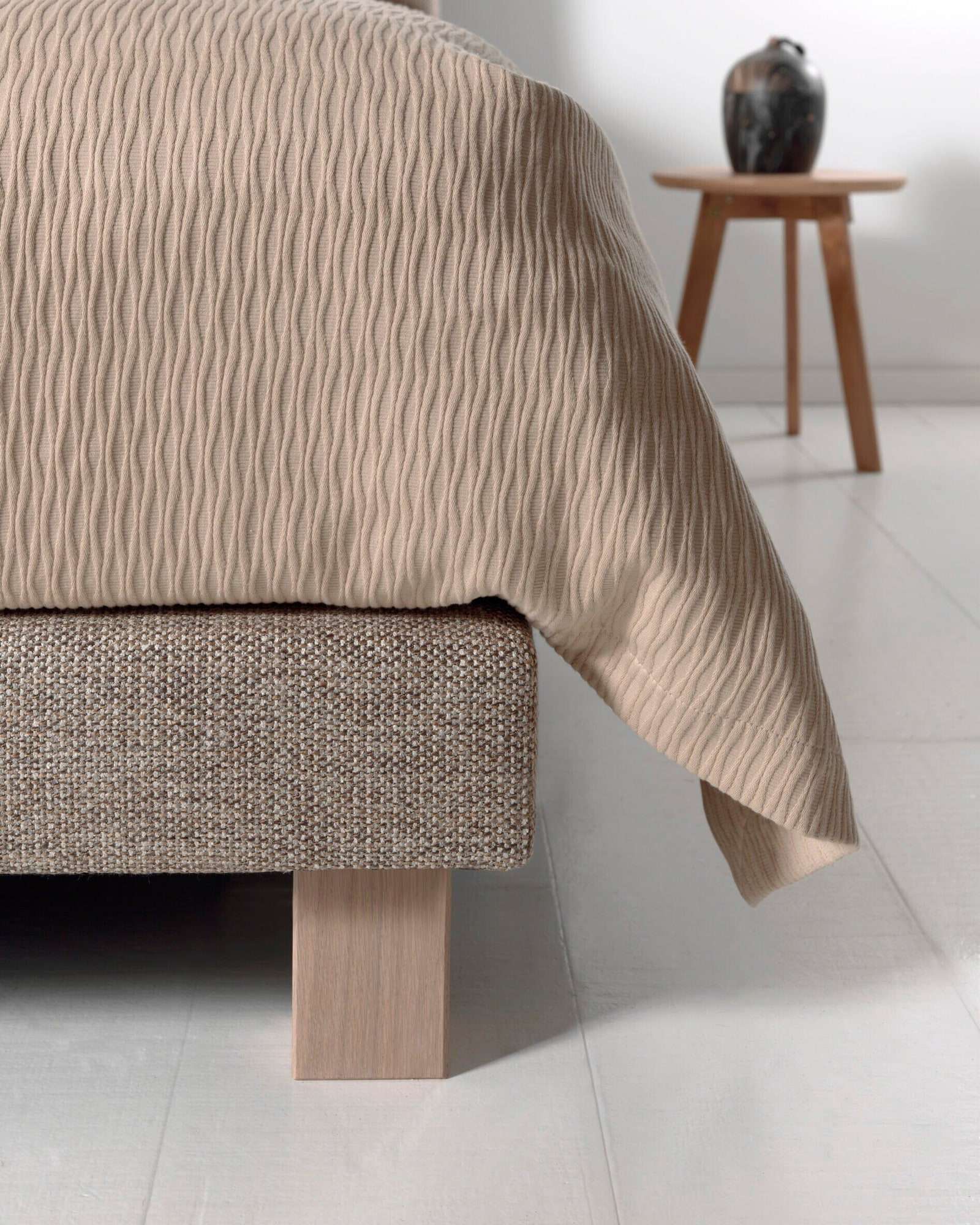 Het voeteneinde van een boxspring op een houten blokpoot, met een golvend dekbed