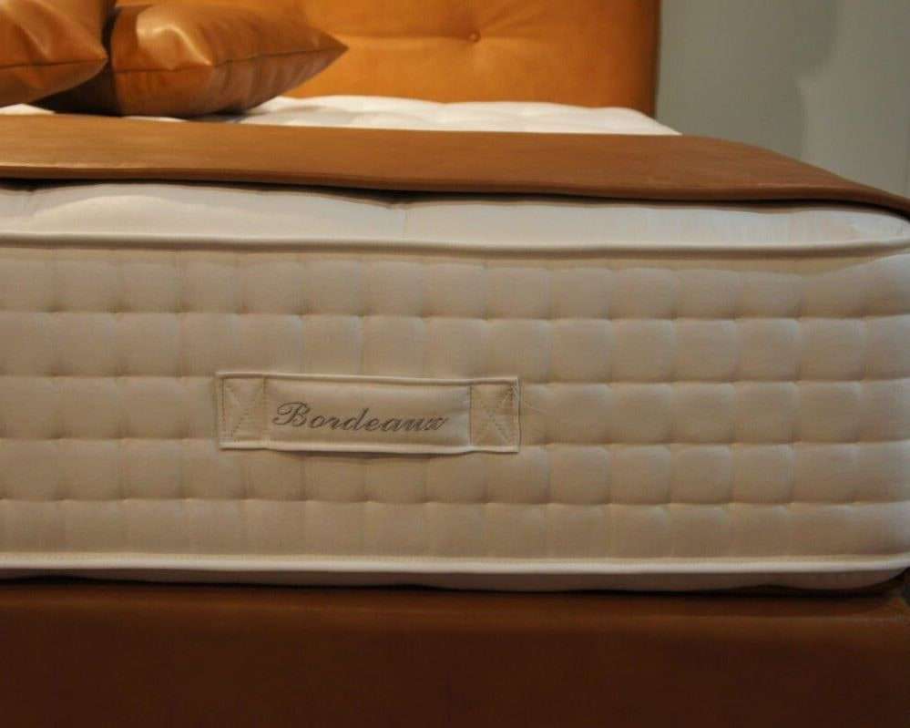 De zijkant van een getufte matras met een geborduurd label, op een cognackleurige boxspring
